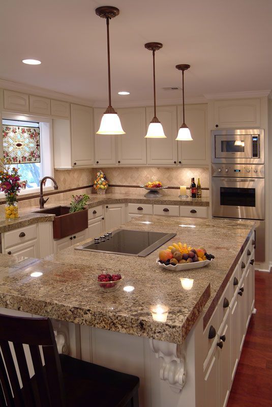 a kitchen with white cabinets and granite counter tops, two pendant lights over the sink