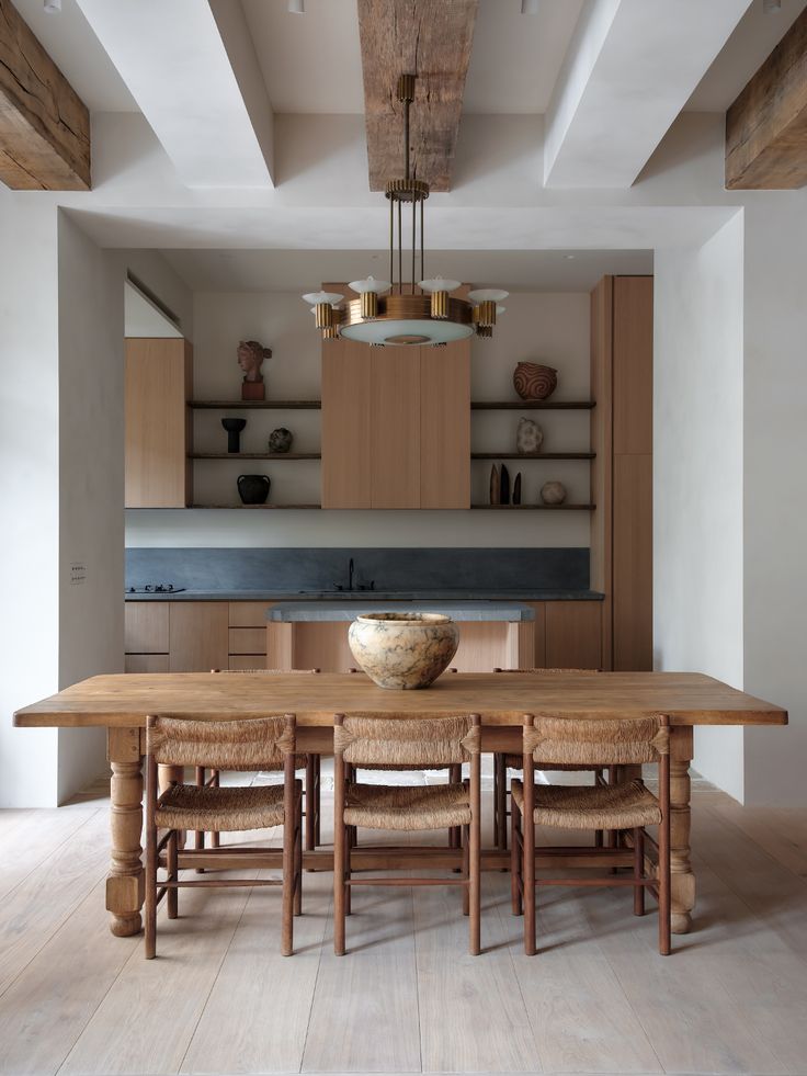 a dining room table with chairs and a bowl on top of it in front of an open kitchen area