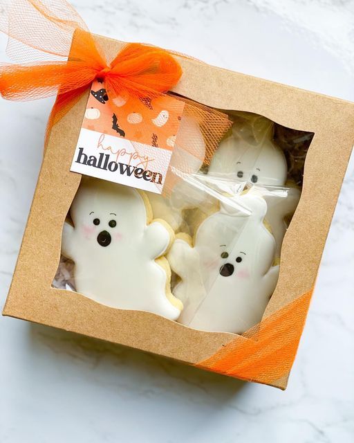 three white ghost cookies in a box with an orange bow on the top and one is inside