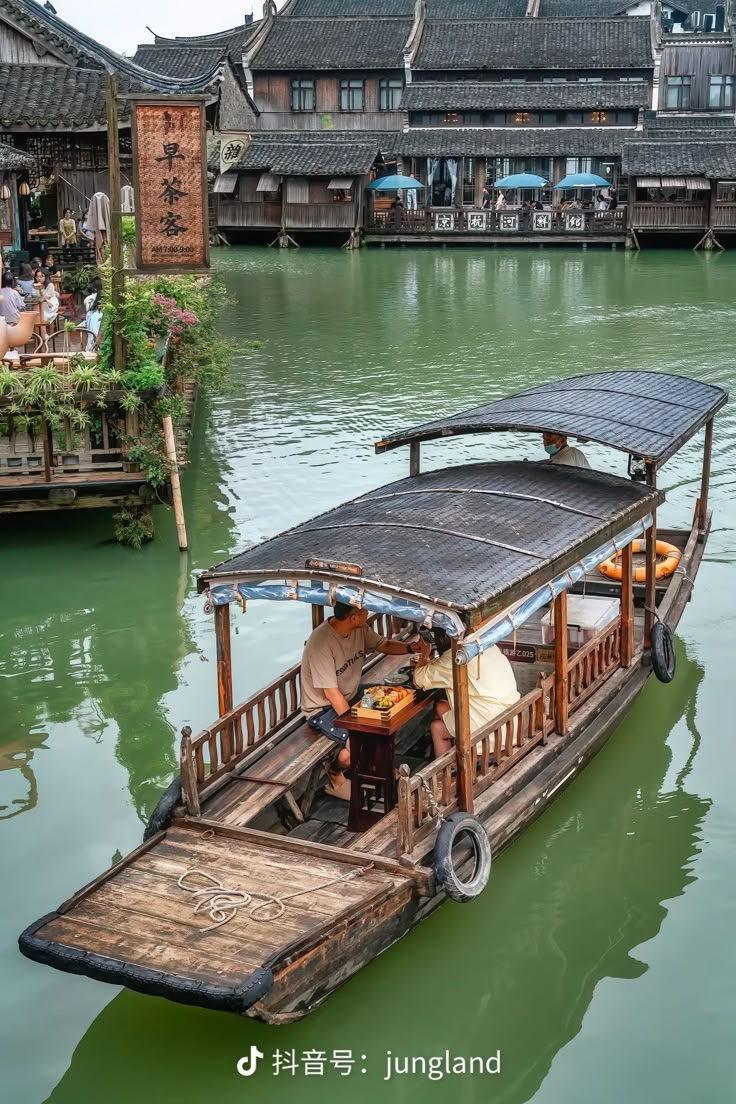 a small boat floating on top of a river filled with water next to wooden buildings