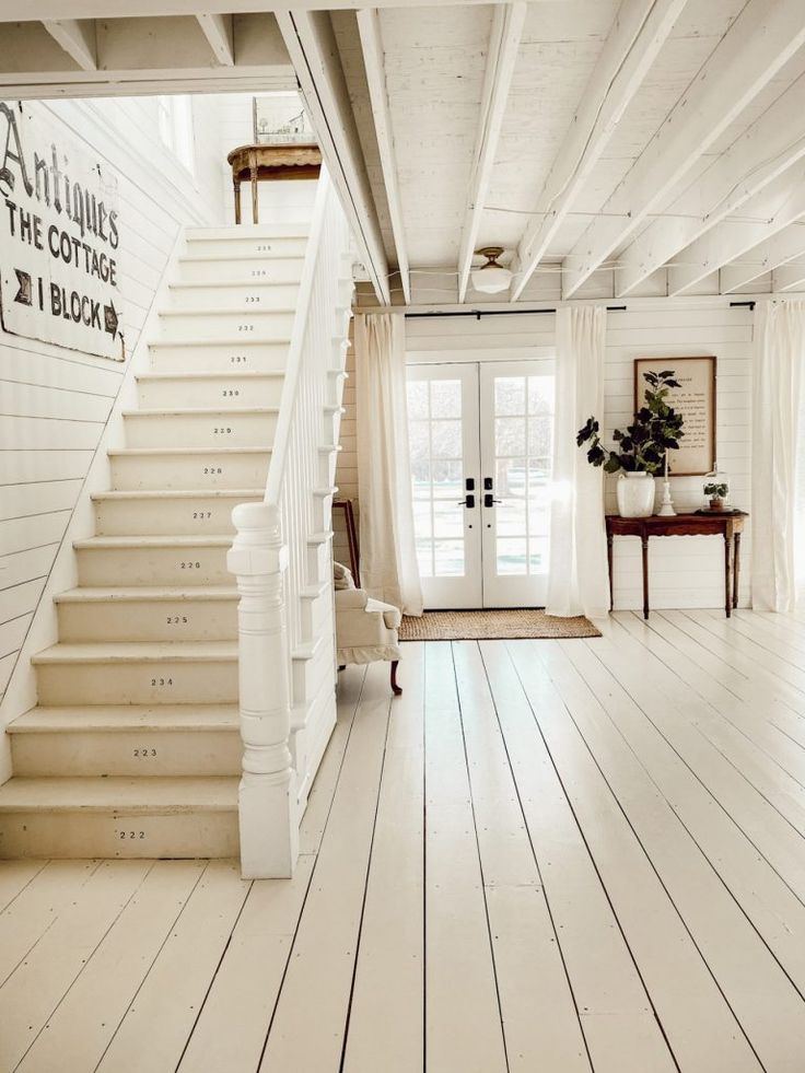 a room with white floors and stairs leading up to the second floor, along with a door that leads to another room