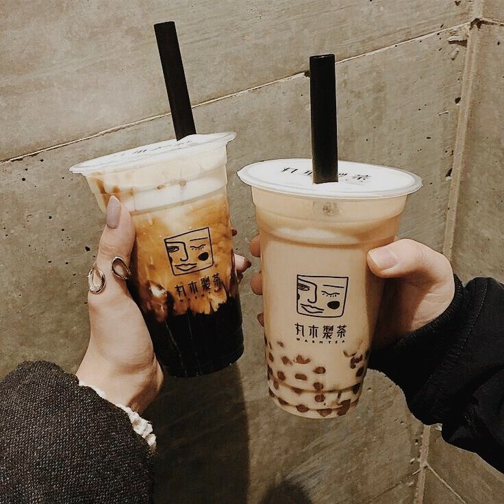 two people holding up cups with drinks in them on the side of a building wall