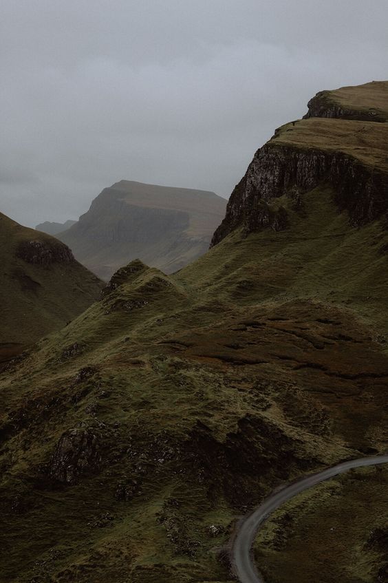 a winding road in the middle of a mountain range on a foggy, cloudy day