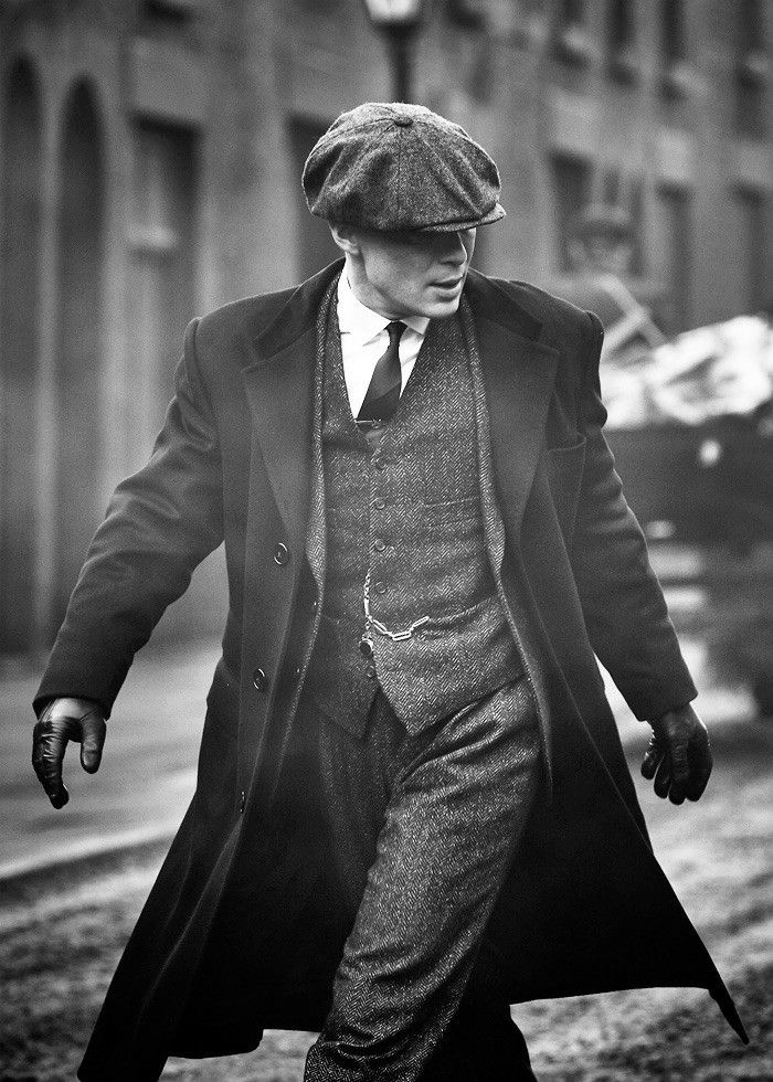 black and white photograph of man walking down the street in an old fashion coat, hat, and tie