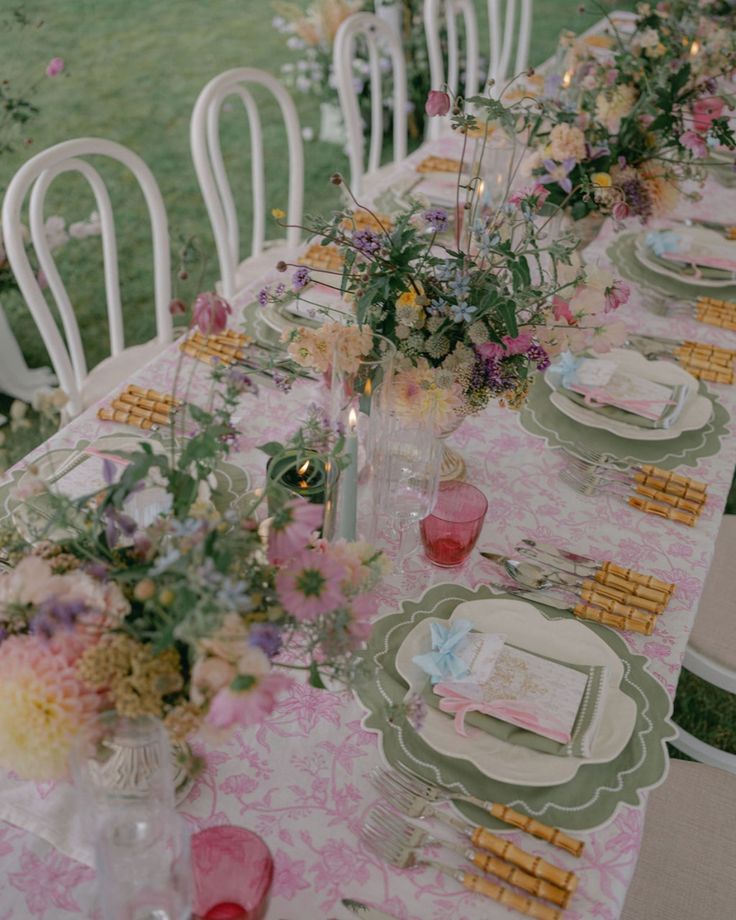 a long table with plates and flowers on it is set for an outdoor dinner party