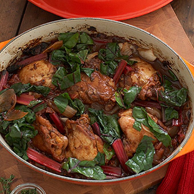 a pot filled with meat and vegetables on top of a wooden table next to a plate