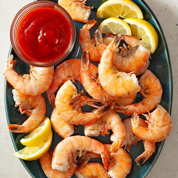 a plate with shrimp, lemon wedges and ketchup next to a bowl of sauce