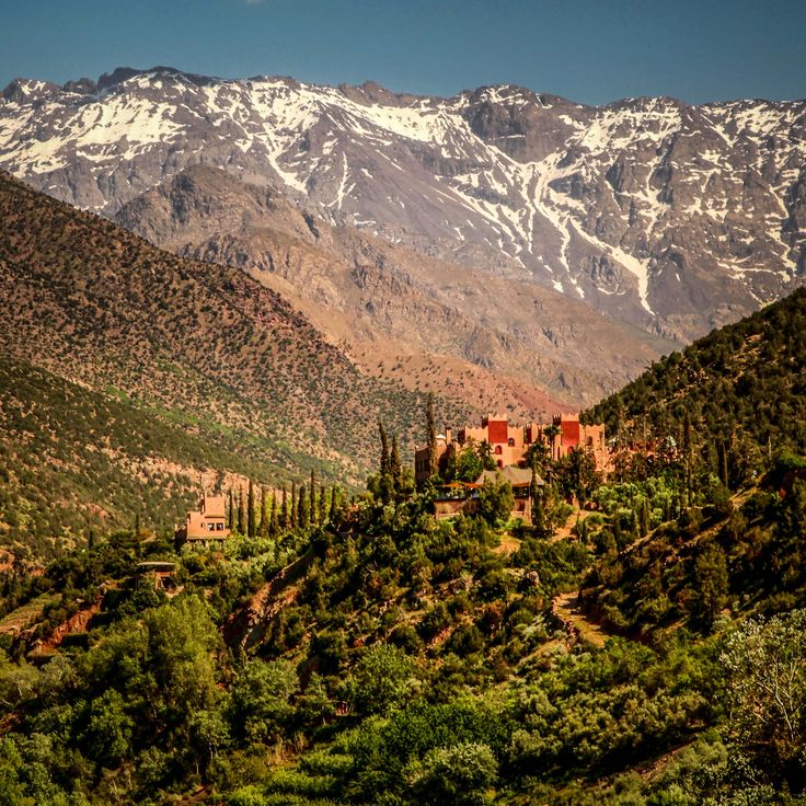 the mountains are covered in snow and green trees, with an old building on top