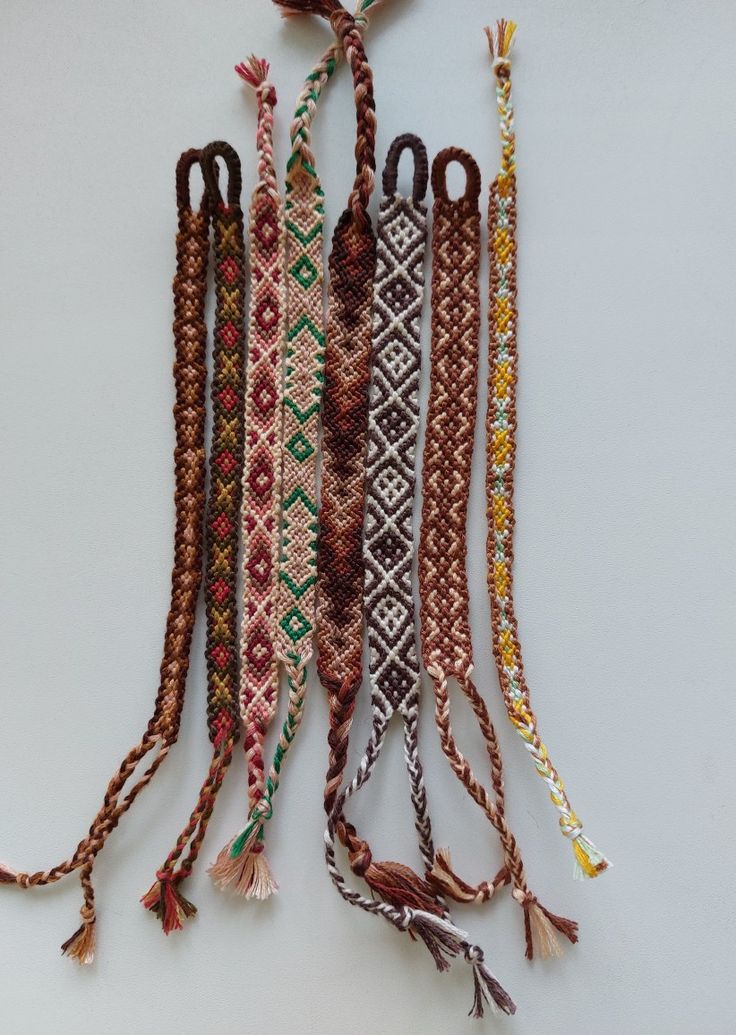 several bracelets are hanging on a white wall with tassels attached to them