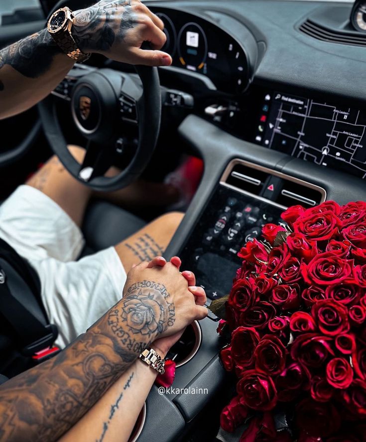 a man driving a car with red roses on the dashboard and his hand in the driver's wheel