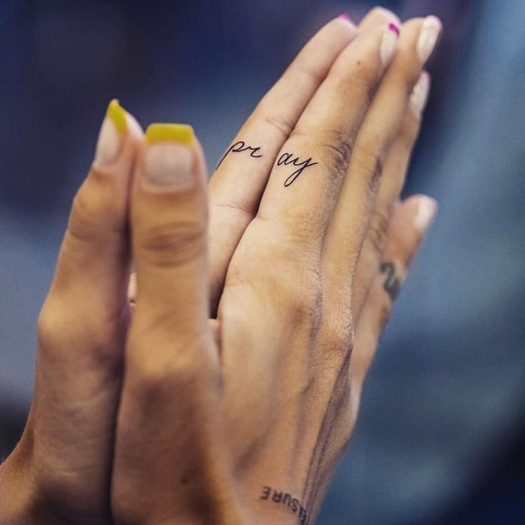 two hands holding each other with tattoos on their fingers and the words pray written on them