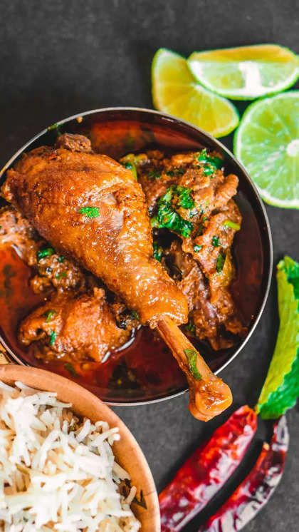 chicken curry served in a bowl with rice, limes and red peppers on the side