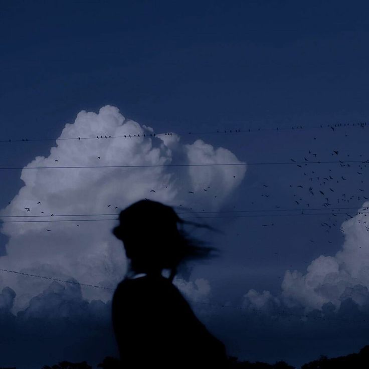 the silhouette of a person standing in front of a cloud with birds flying over it