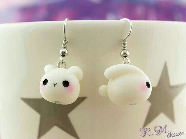 a pair of white teddy bear earrings with black eyes and nose piercings sitting on top of a coffee cup