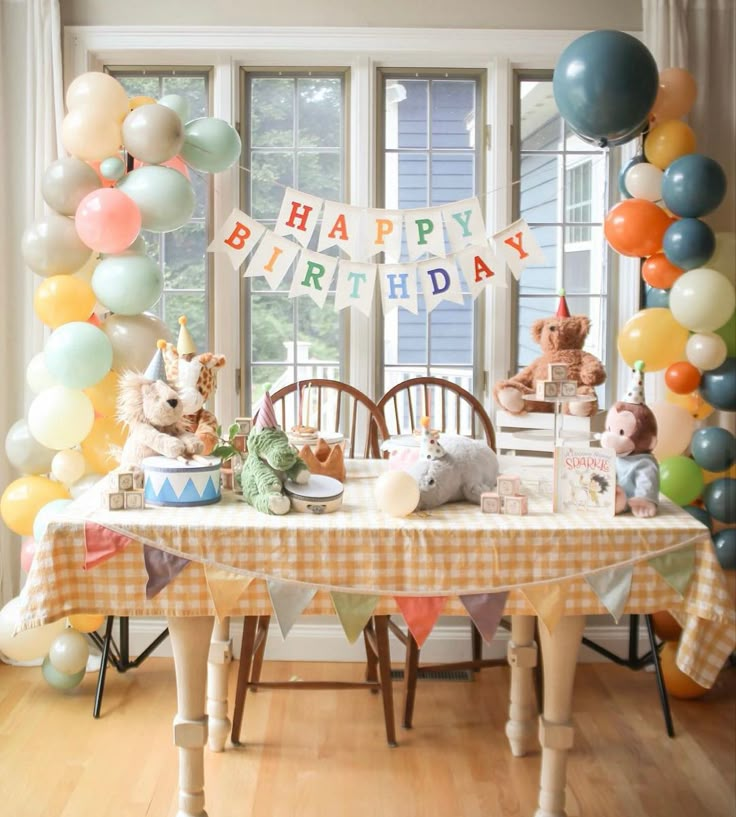 a birthday party with balloons and stuffed animals on the table in front of a window