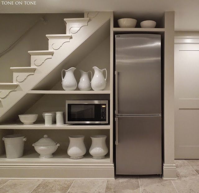 a refrigerator and shelves in a kitchen with white dishes on the shelf next to it