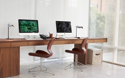 two computer monitors sitting on top of a wooden desk next to each other in front of a window