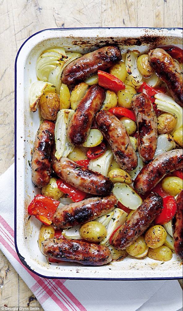 sausages and vegetables in a baking dish on a wooden table with a striped napkin