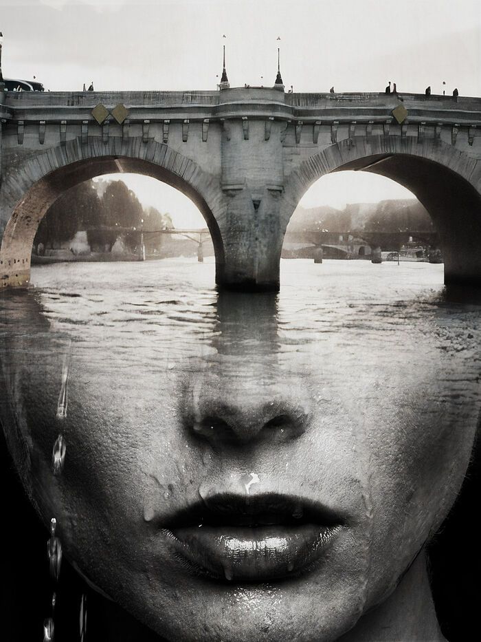 a woman's face is reflected in the reflection of an old bridge over water