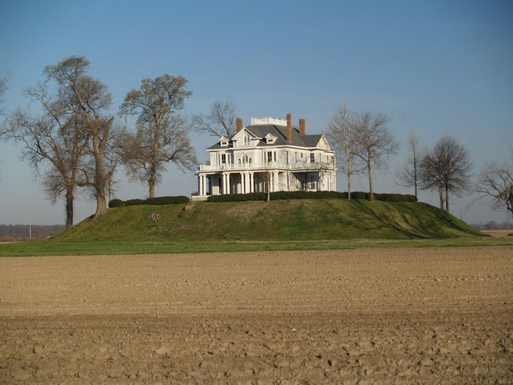 a large white house sitting on top of a lush green hillside next to trees and an empty field