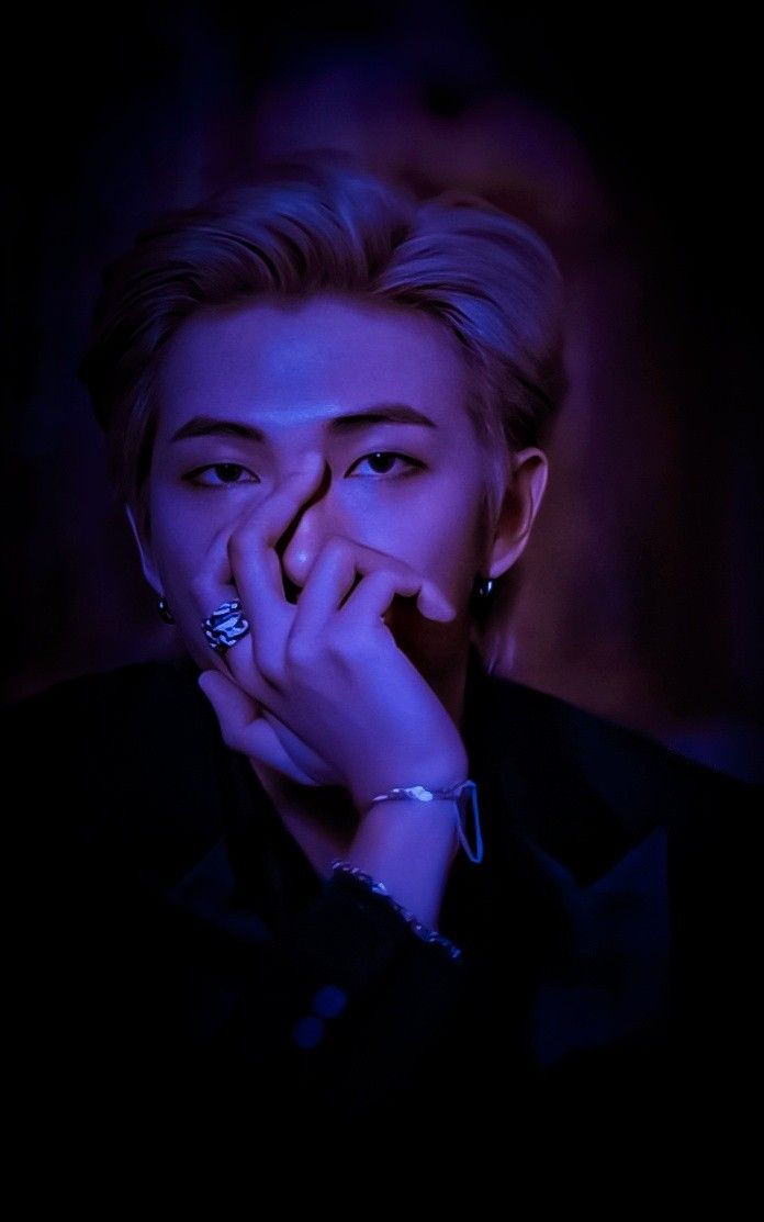 a person with their hands on their face in the dark, looking at something while holding his hand to his mouth