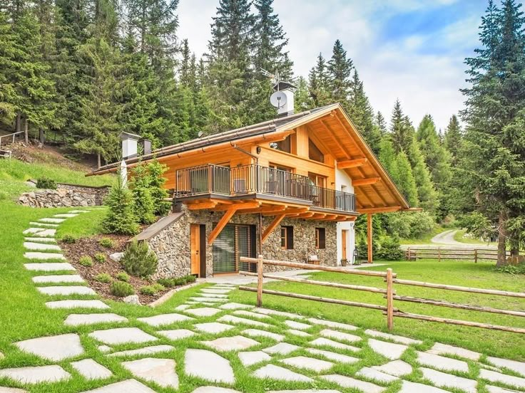 a house in the woods with stone walkways and green grass on both sides, surrounded by pine trees