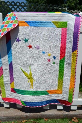 a colorful quilt on a white fence with stars in the sky and birds flying around