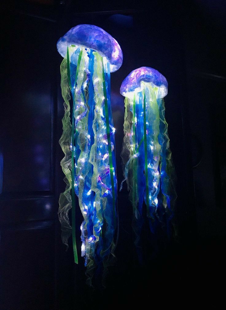 two blue and green jellyfish lights hanging from the side of a wall in a dark room