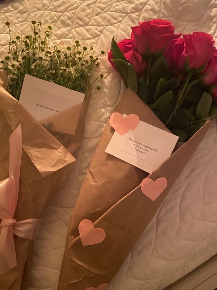 two brown paper bags with pink flowers and hearts on them sitting on a white bed