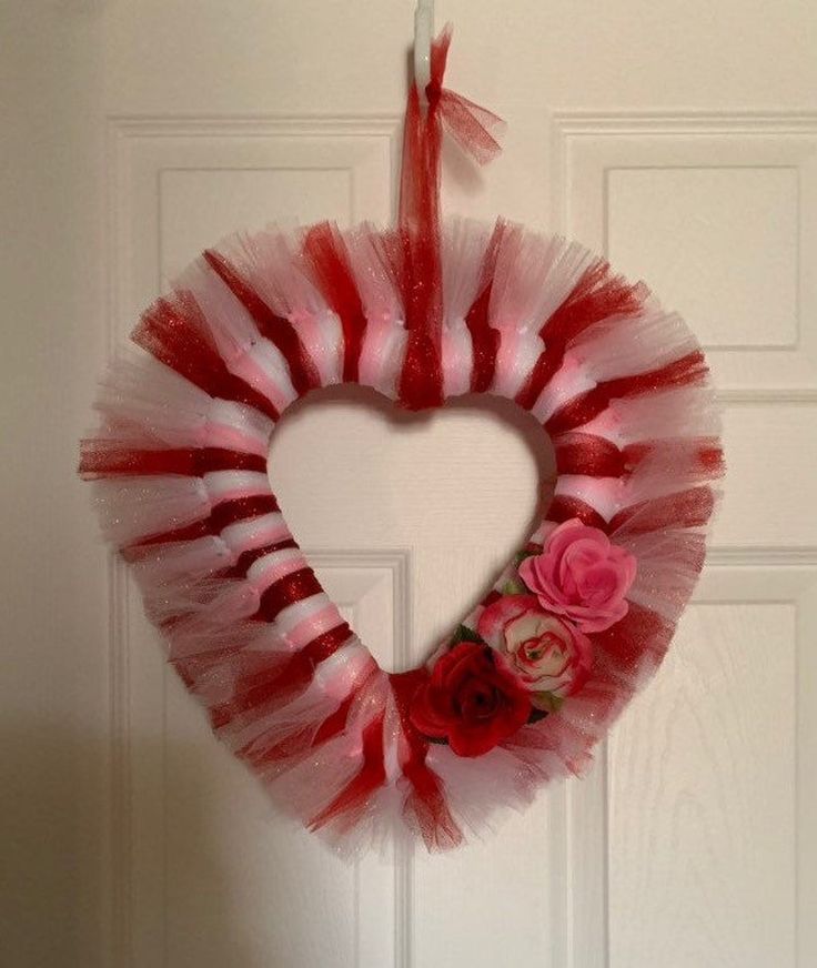 a heart shaped wreath hanging on the front door with red and white tulle skirt