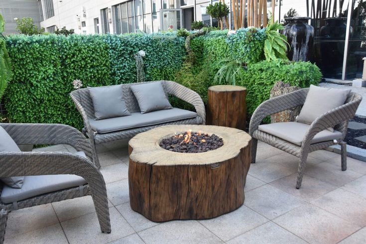 a fire pit sitting on top of a wooden table next to two chairs and a tree stump