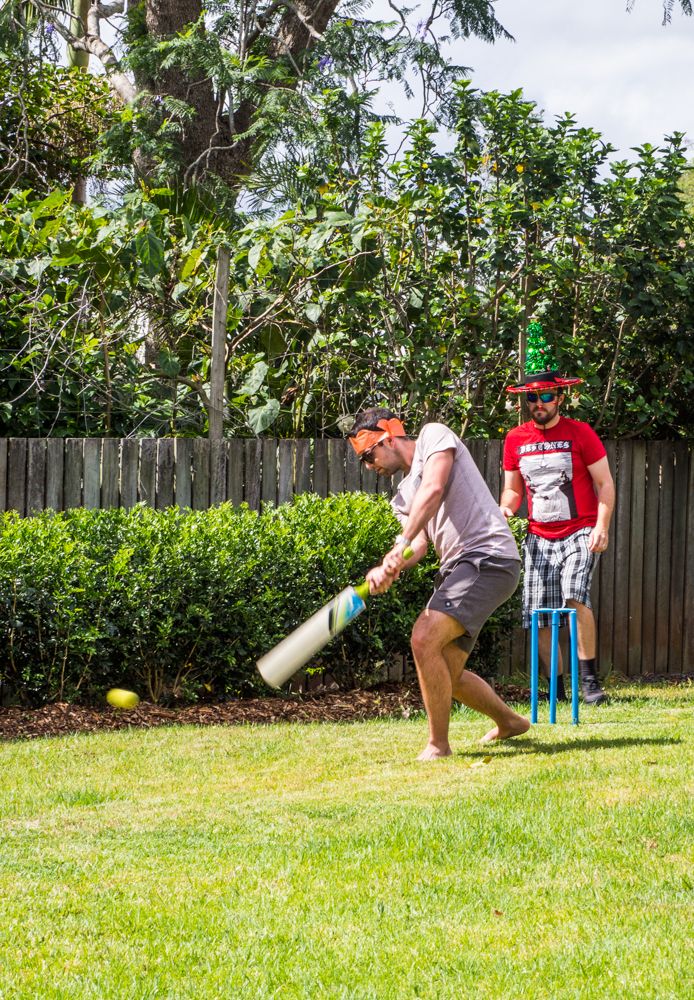 two men are playing baseball in the yard with one holding a bat and the other swinging at a ball