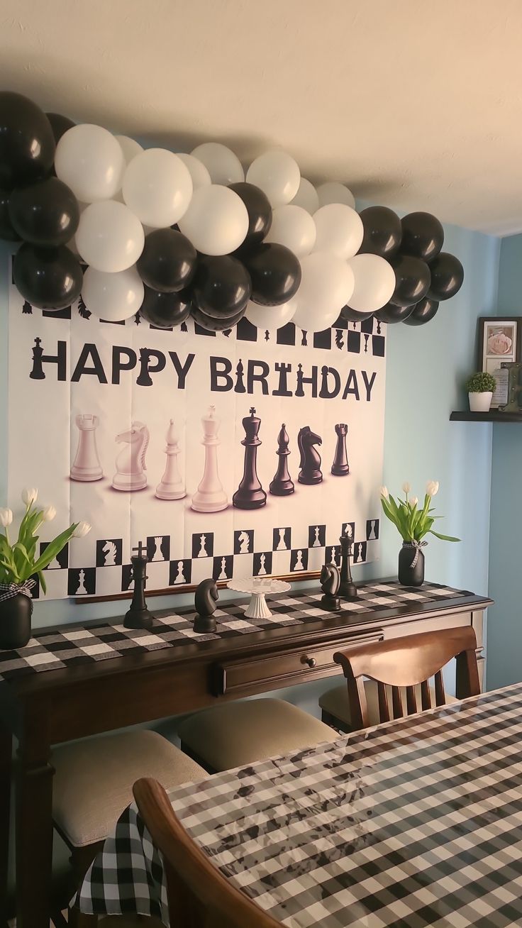 a birthday party with black and white balloons hanging from the ceiling, chess board on the wall