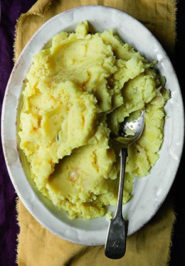 mashed potatoes in a white bowl with a spoon on a purple and yellow table cloth