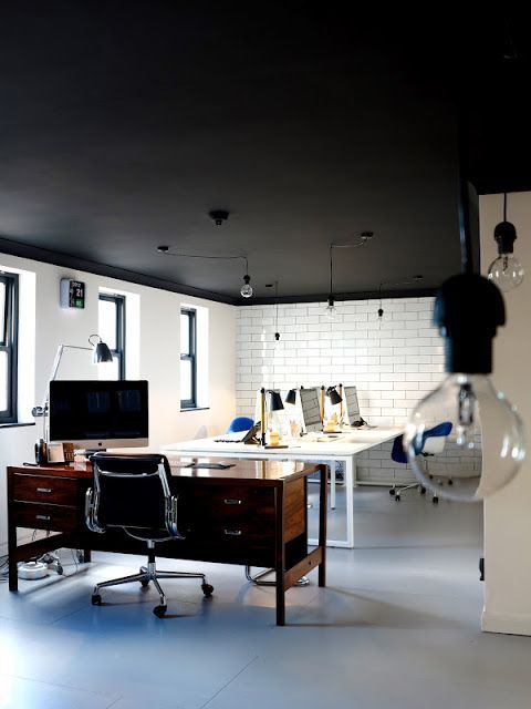 an office with two desks and a computer monitor on top of it, in front of windows