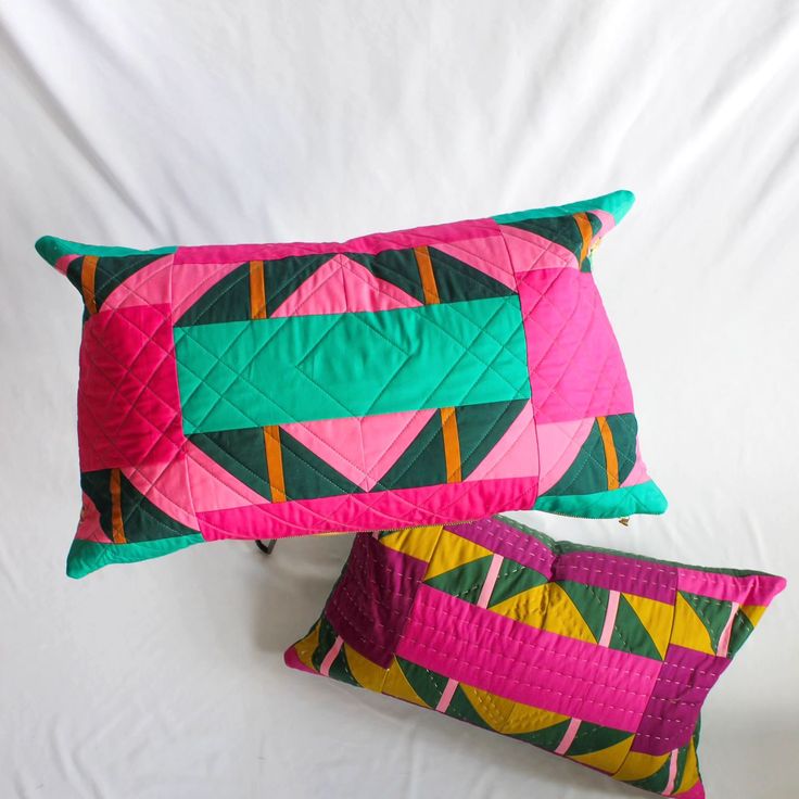 two colorful pillows sitting next to each other on a bed