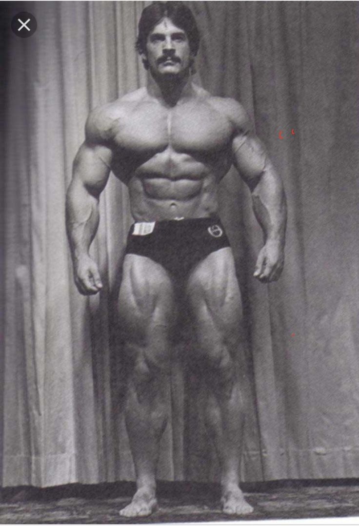 a man standing in front of a curtain posing for the camera with his muscles exposed