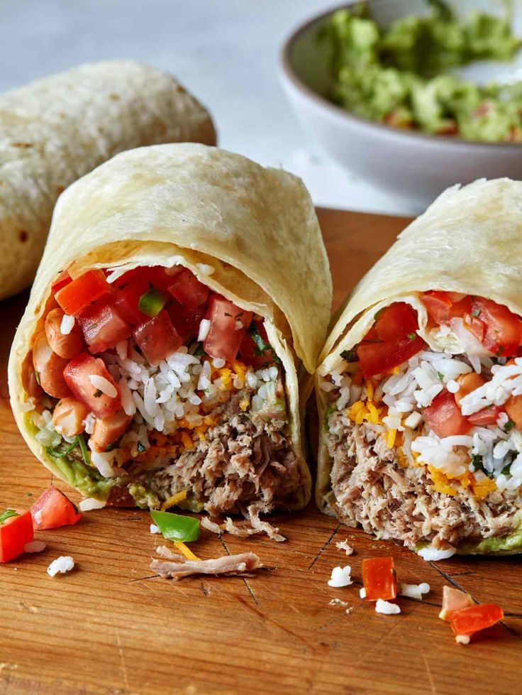 two burritos cut in half on a cutting board with guacamole and salsa