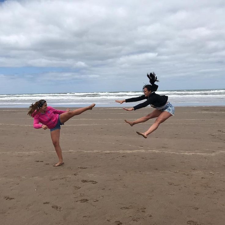 two girls are playing with a frisbee on the beach while another girl jumps in the air