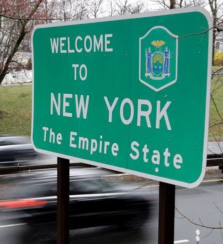 a welcome to new york sign in front of a street with cars passing by on the road