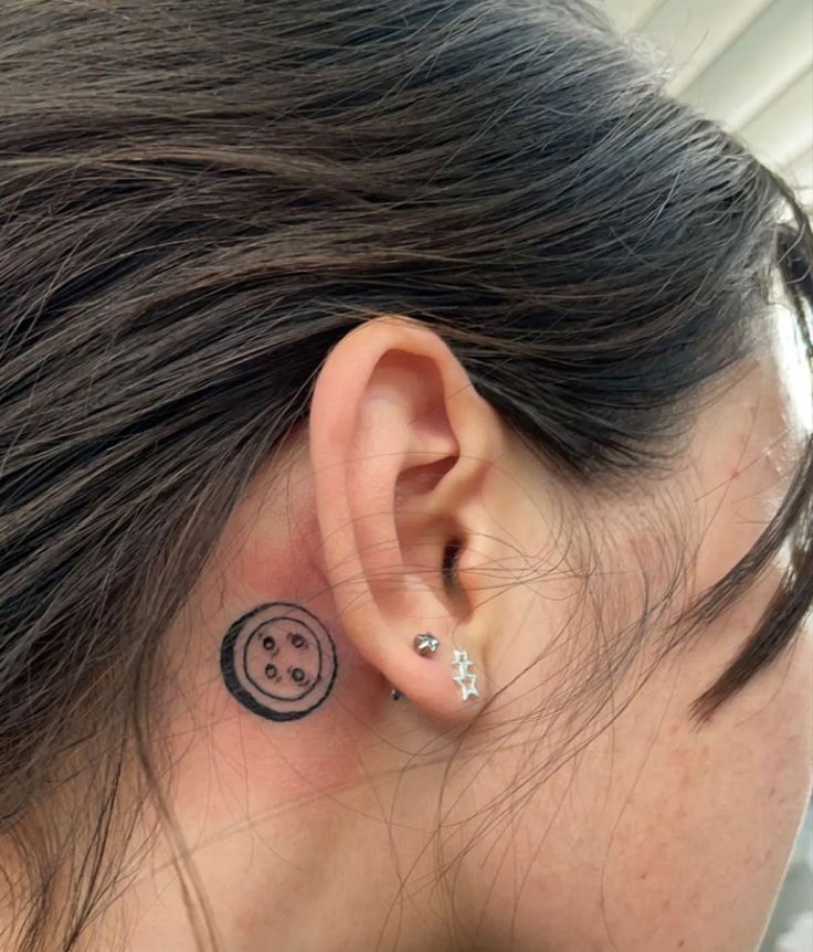 a woman with a smiley face tattoo on her left side behind the ear and behind the ear is an ear pin