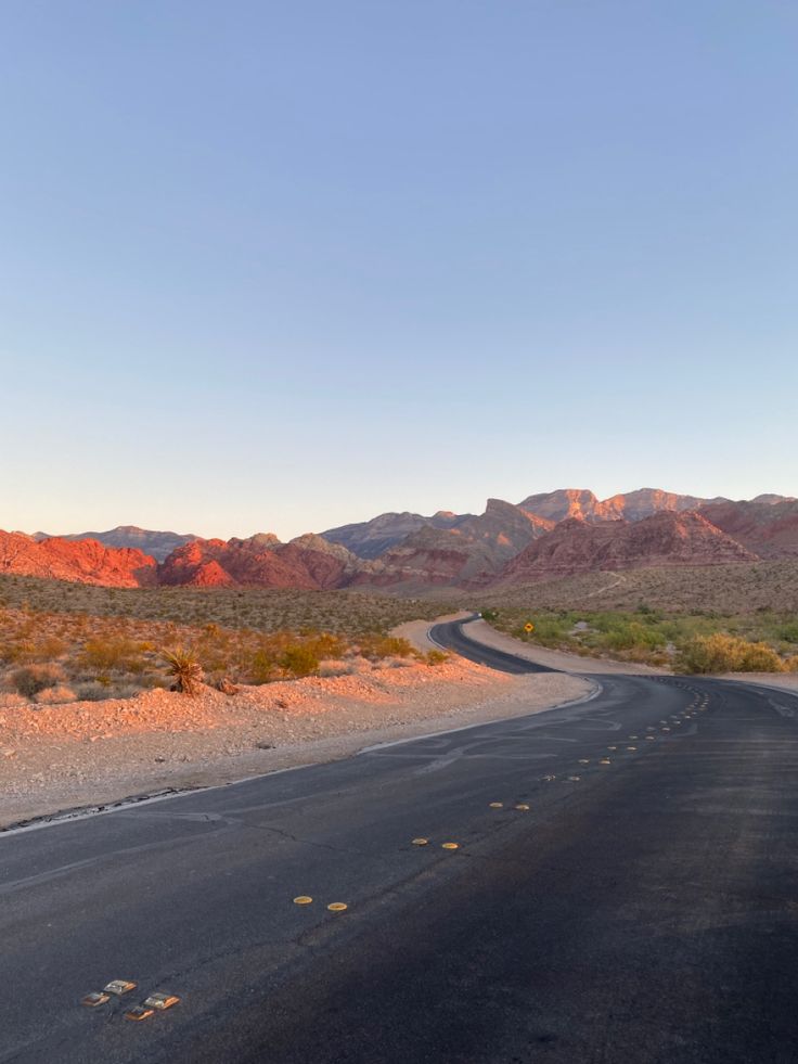 an empty road in the desert with mountains in the backgrounnd and blue sky