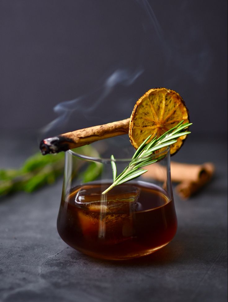 a glass filled with liquid next to a cinnamon stick and some green leaves on the table