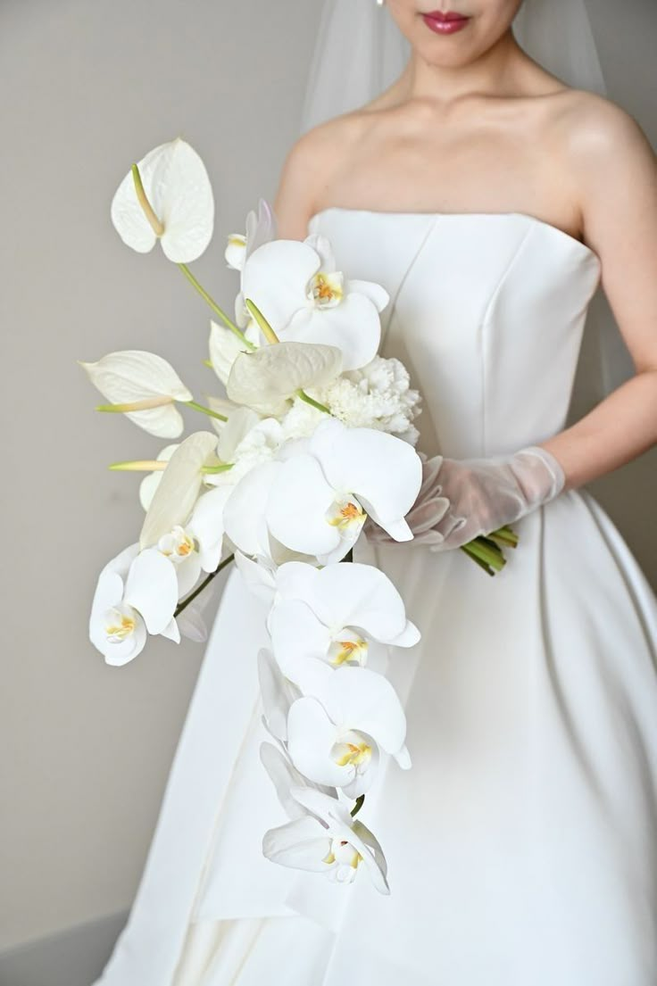 a woman in a white wedding dress holding a bouquet of orchids and lilies