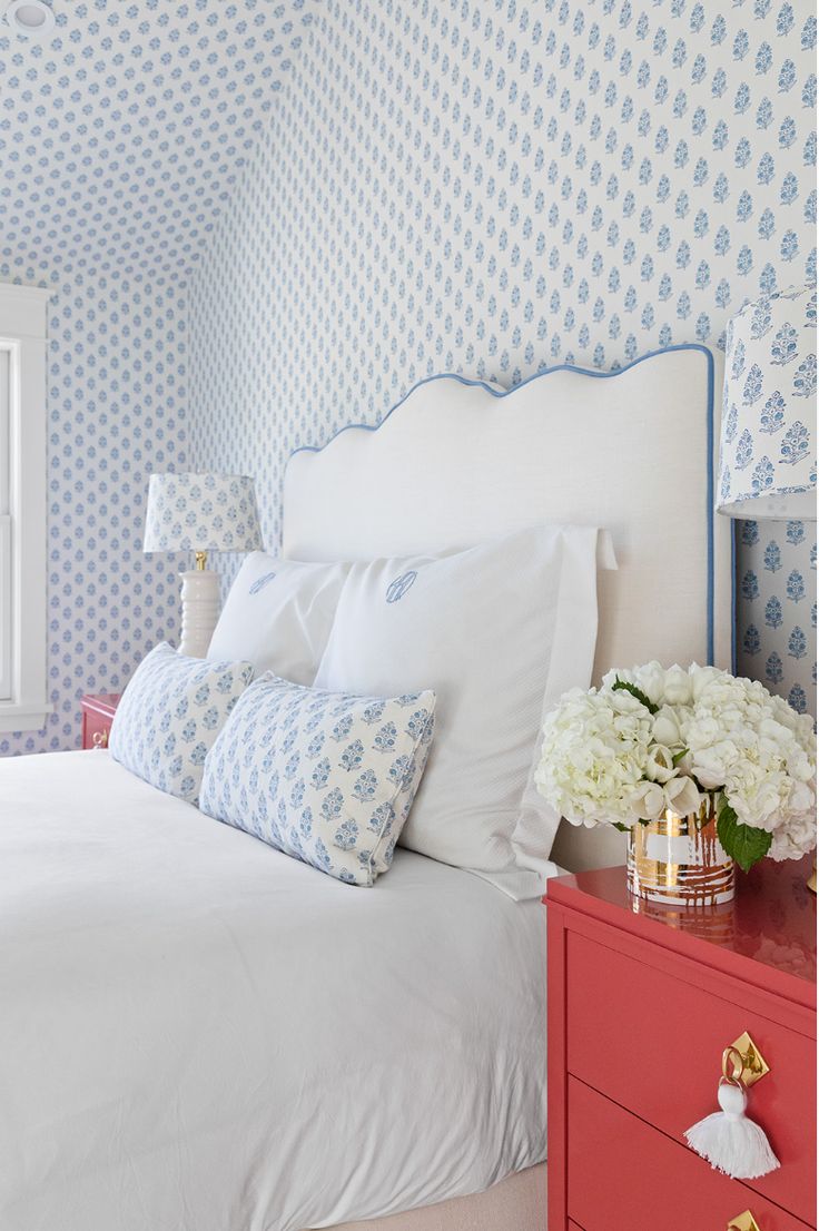 a white bed with blue and white wallpaper in a bedroom next to a window