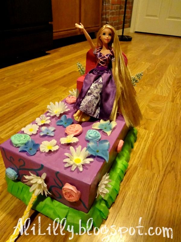 a barbie doll sitting on top of a purple and green cake with flowers in it