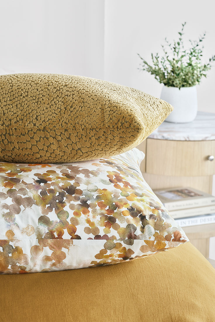 three pillows stacked on top of each other in front of a nightstand with a potted plant