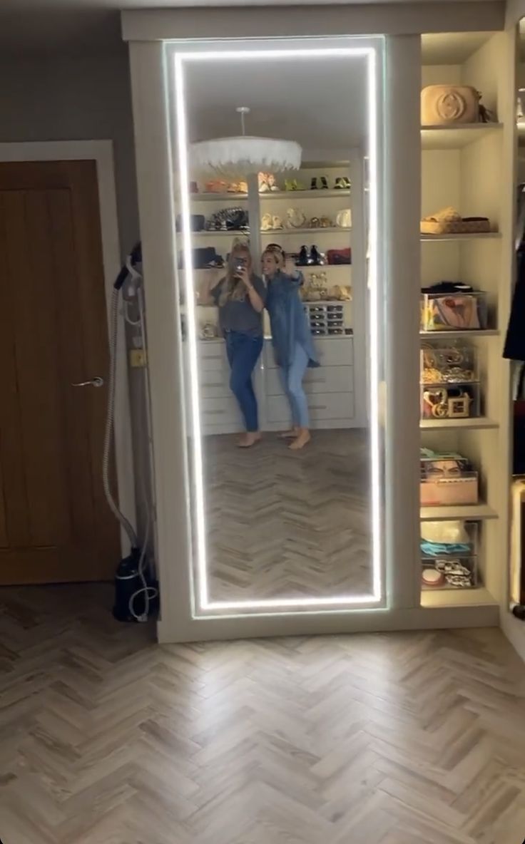 two women standing in front of a large mirror