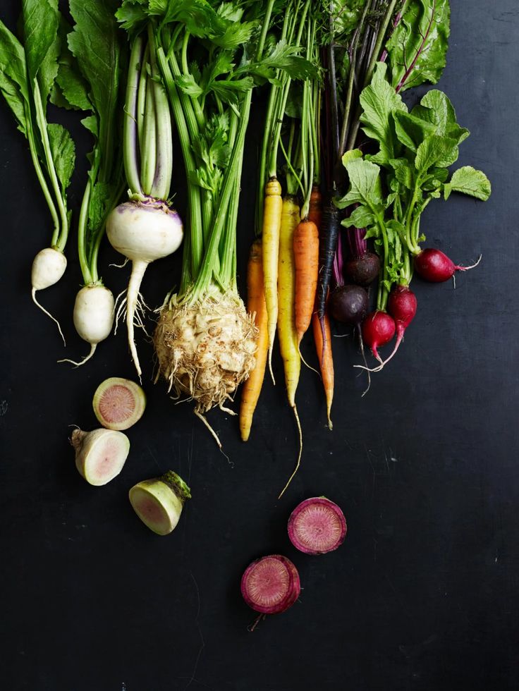 there are many different types of vegetables on the black surface, including carrots, radishes, turnips and celery