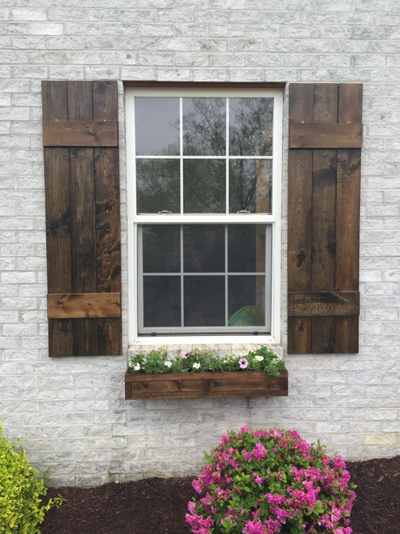 a white brick building with wooden shutters and flowers in the window box next to it